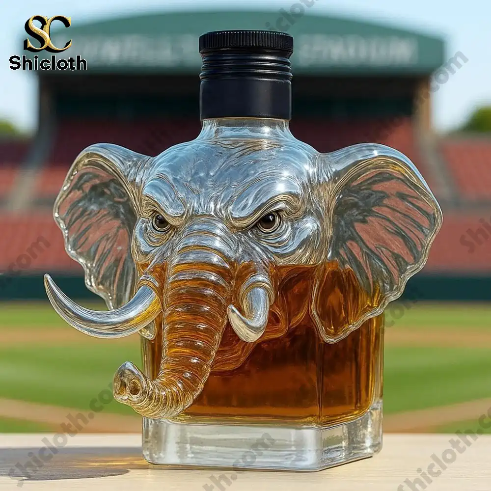 University of Alabama Crimson Tide Whiskey Bottle 3 Glass elephant-shaped liquor bottle filled with brown liquid placed on a table in a stadium background!