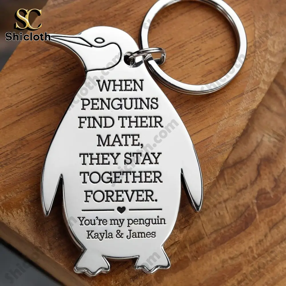 Penguin shaped keychain engraved with a love quote resting on wooden surface.