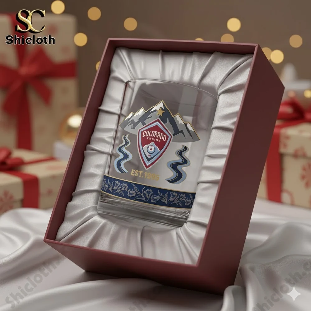 A Colorado Rapids glass displayed inside a cushioned gift box with holiday lights and wrapped presents in the background!