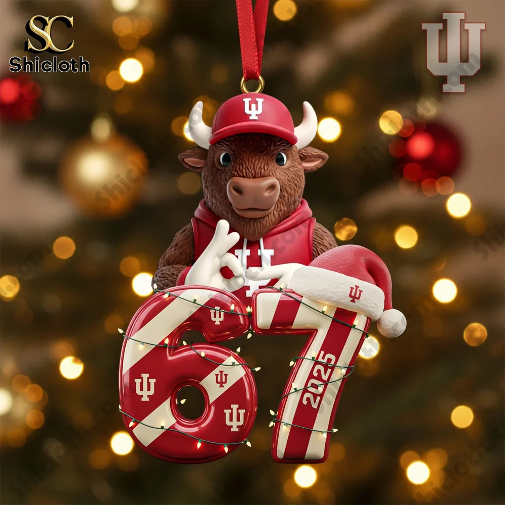 A holiday mascot ornament wearing red apparel holding the number sixty seven before a Christmas tree!