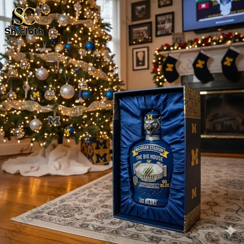 A Michigan Stadium whiskey bottle displayed in front of a Christmas tree decorated with Michigan-themed ornaments.