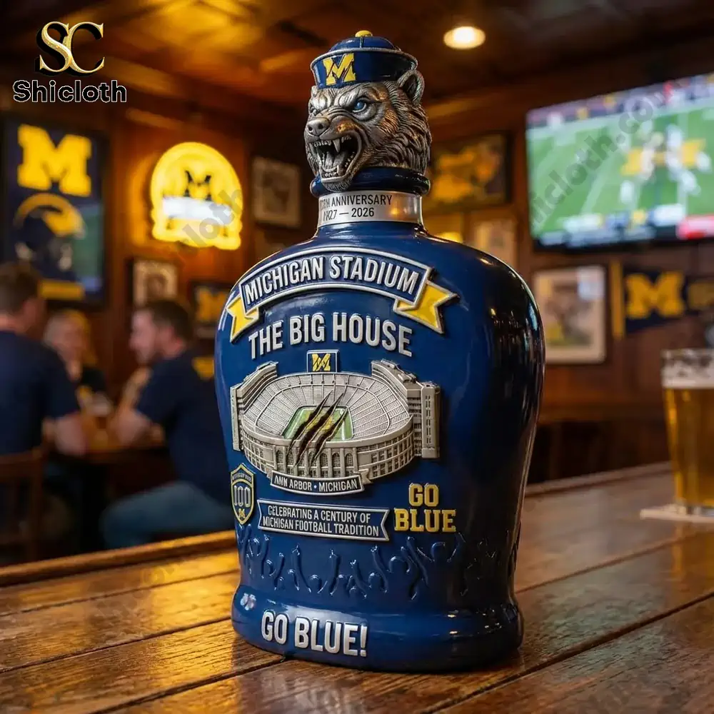 A Michigan Stadium whiskey bottle on a bar counter with Michigan-themed decor and a game playing in the background.