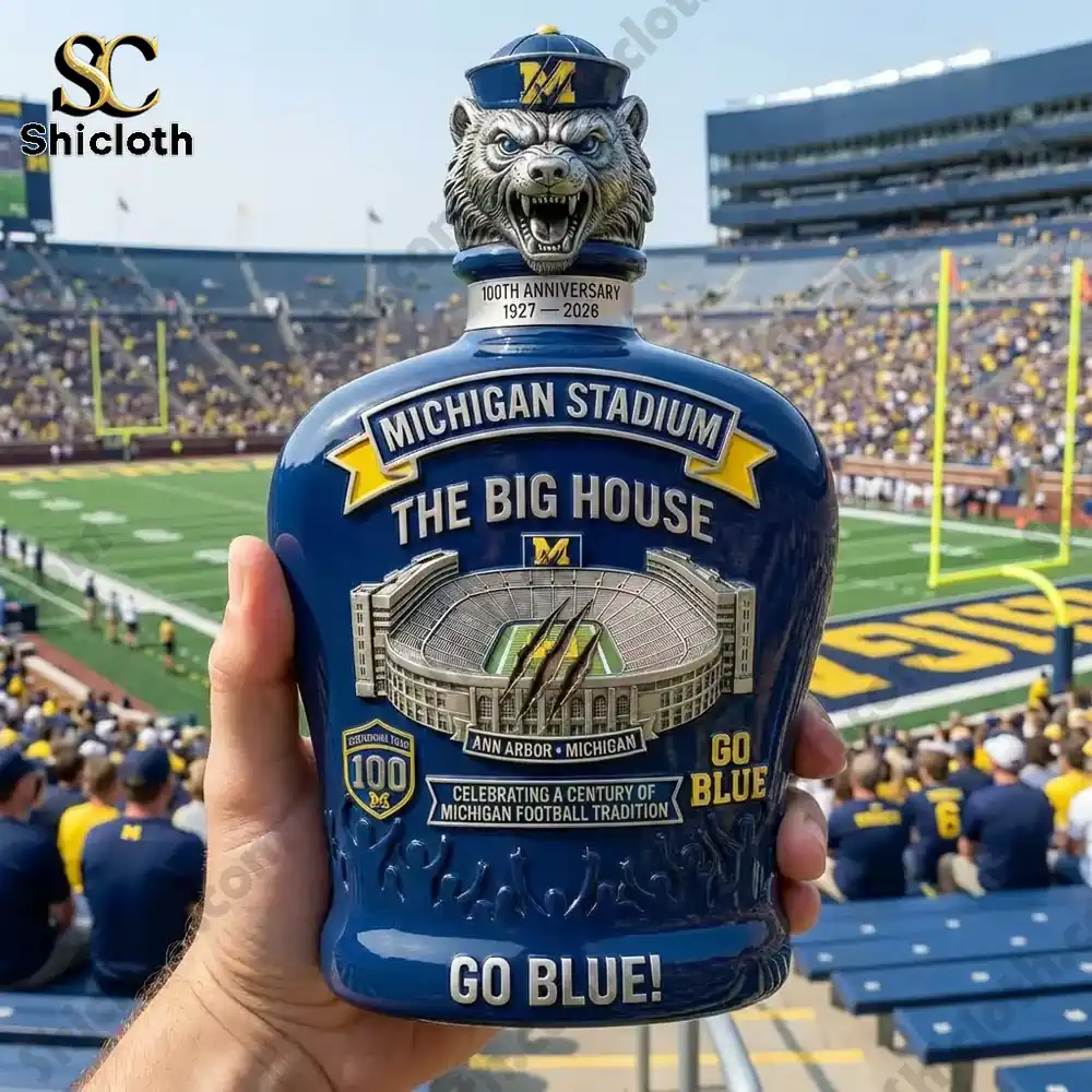 Michigan Stadium 100th Anniversary Whiskey Bottle 4 A Michigan Stadium whiskey bottle held up against a backdrop of the Michigan football game.