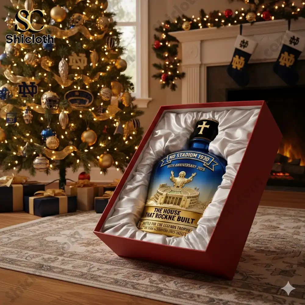 A bottle of whiskey with a blue and gold design, featuring Notre Dame's 1930 stadium anniversary logo, set against a Christmas tree background with gifts and a fireplace.