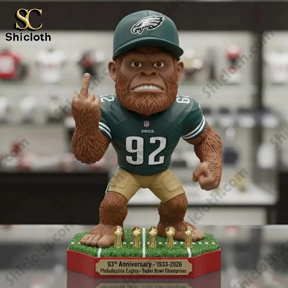 A hairy creature figurine wearing a green Philadelphia Eagles jersey with number 92 and a team cap while showing a middle finger gesture on a base with gold trophies.