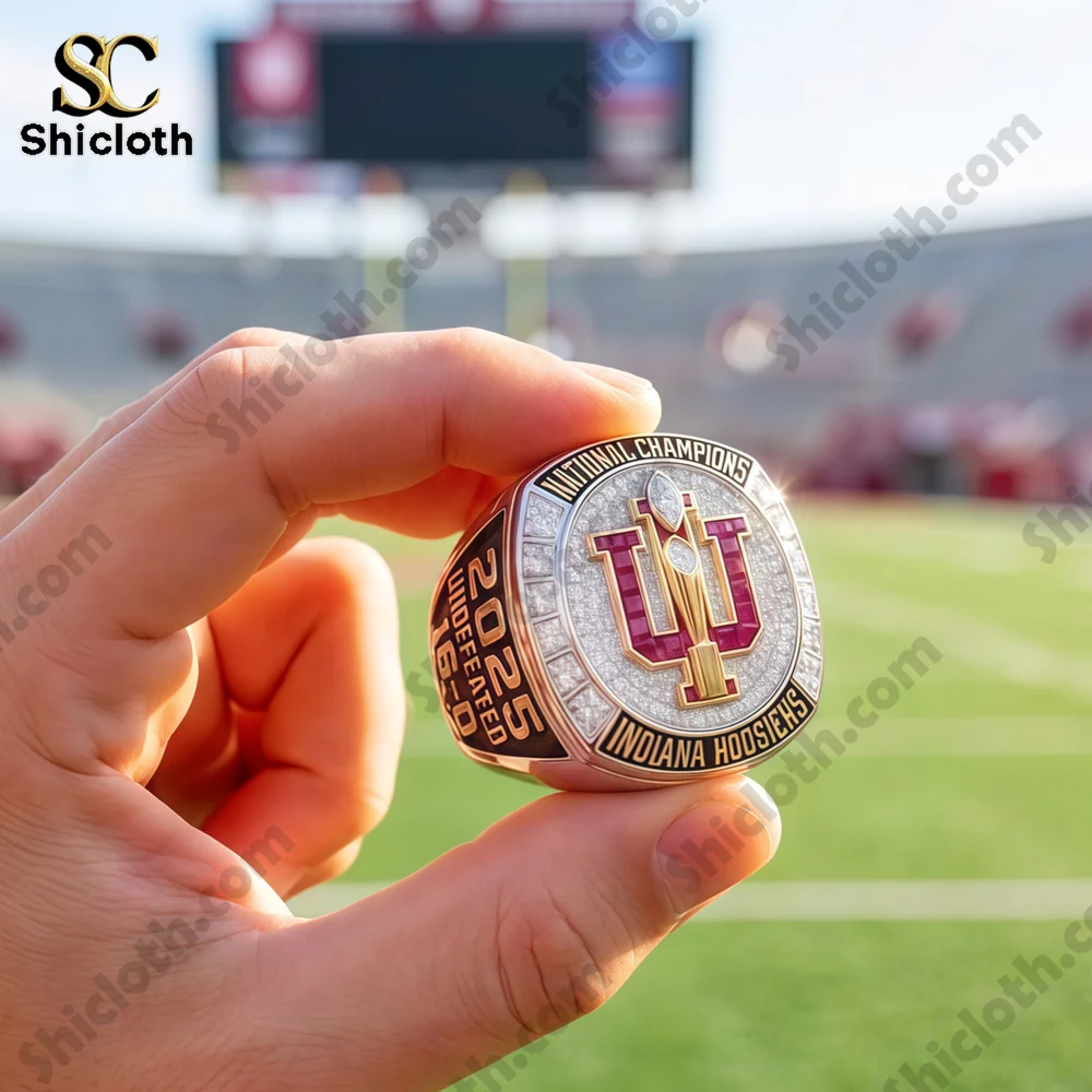 A person holding the Indiana Hoosiers 2025 National Championship ring with a blurred football stadium in the background.
