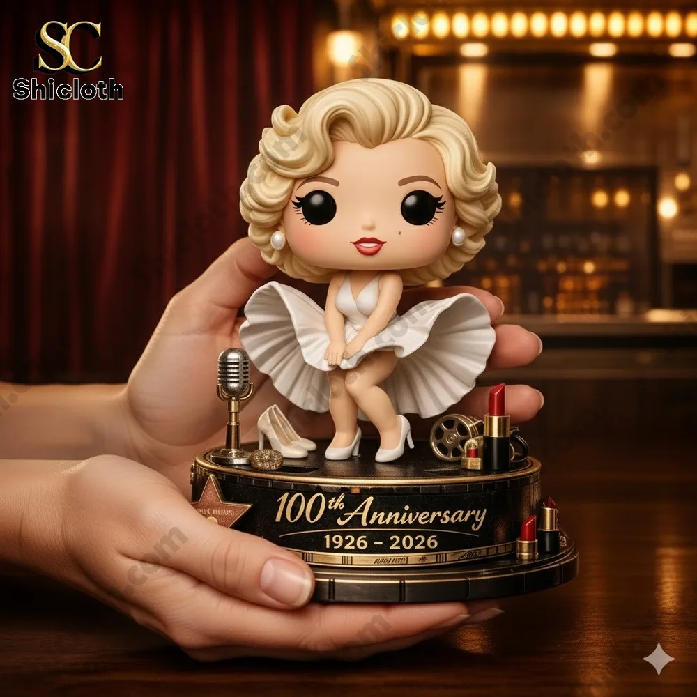 A collectible figurine of a blonde woman in a white dress celebrating the 100th anniversary 1926–2026 held in hands on a stage background.