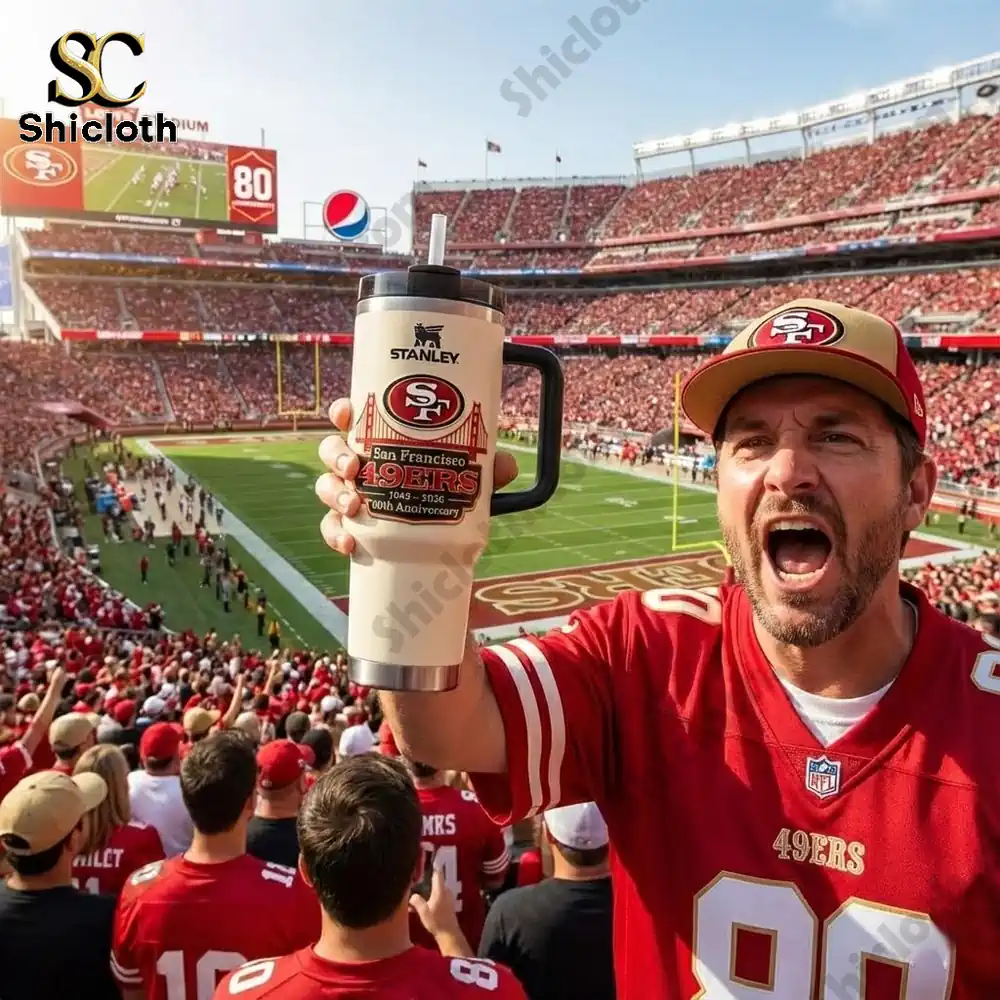 Football fan holding Stanley San Francisco Forty Niners mug inside a stadium.
