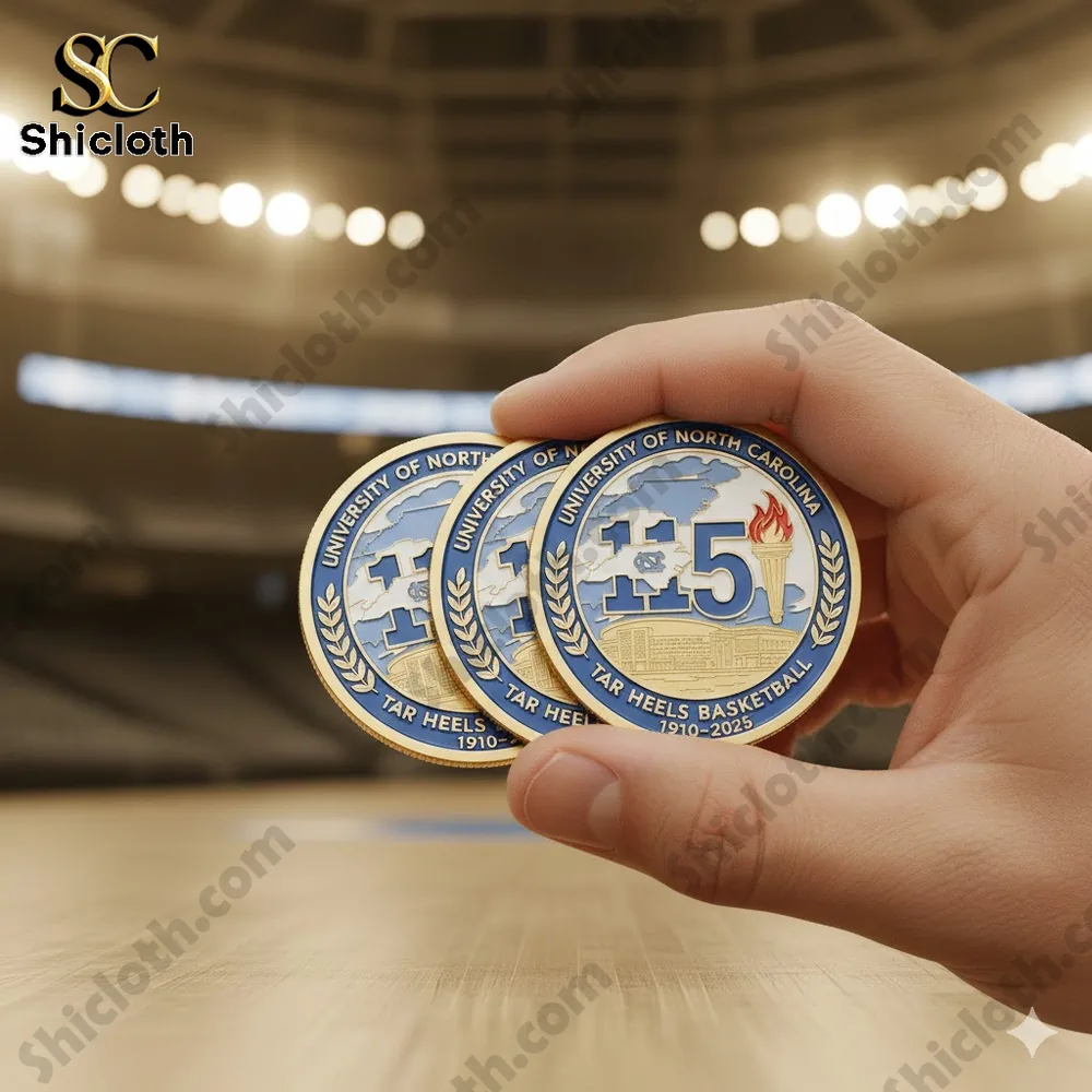 A hand holding three University of North Carolina Tar Heels basketball commemorative coins inside an indoor arena!