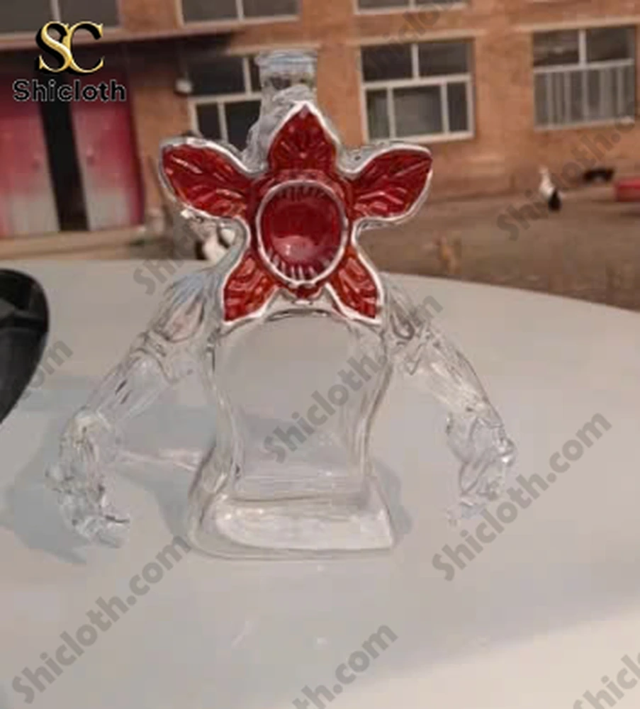 Clear Demogorgon shaped glass bottle with red flower head placed on a white surface outdoors