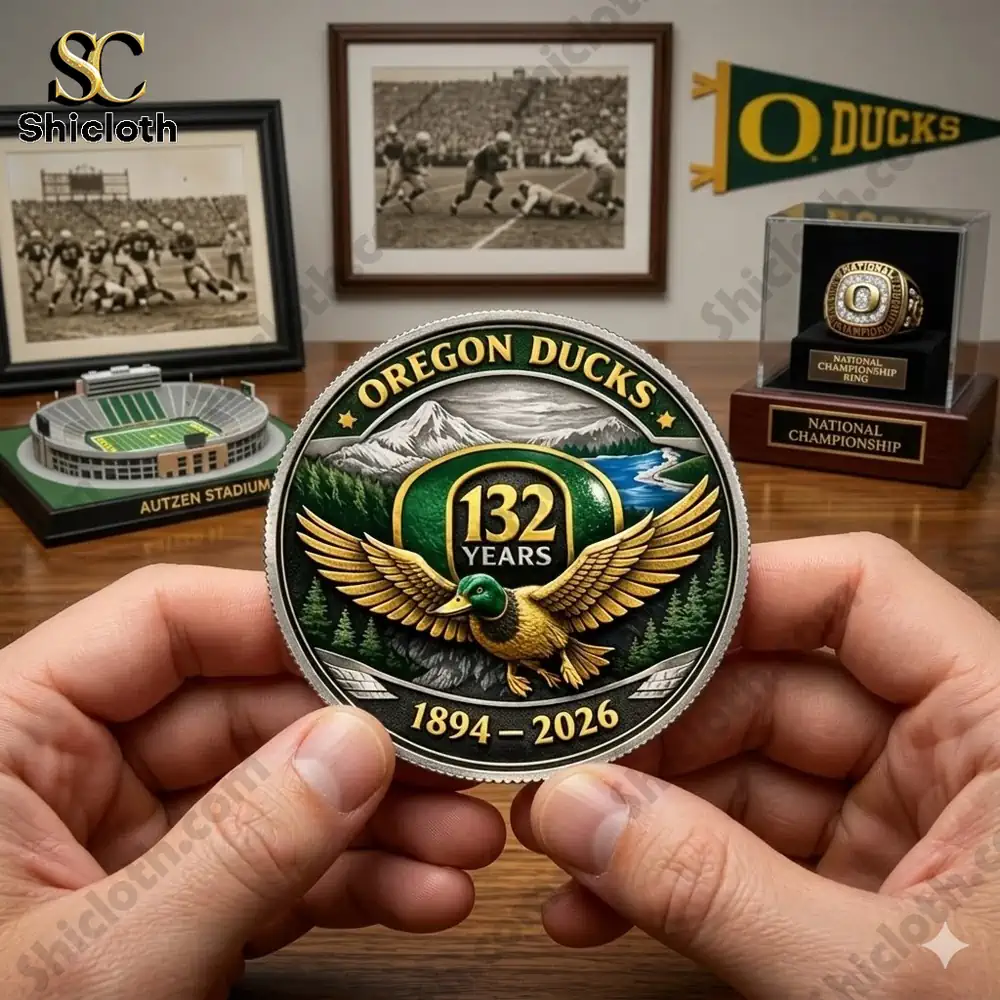 Hands holding Oregon Ducks anniversary coin with stadium model and team memorabilia in background!