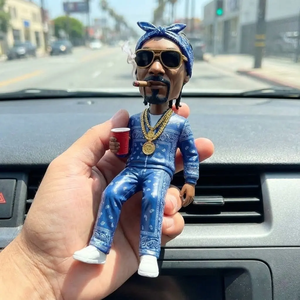 A person holding a Snoop Dogg bobblehead with a blue tracksuit and a cigar, sitting on a car dashboard.