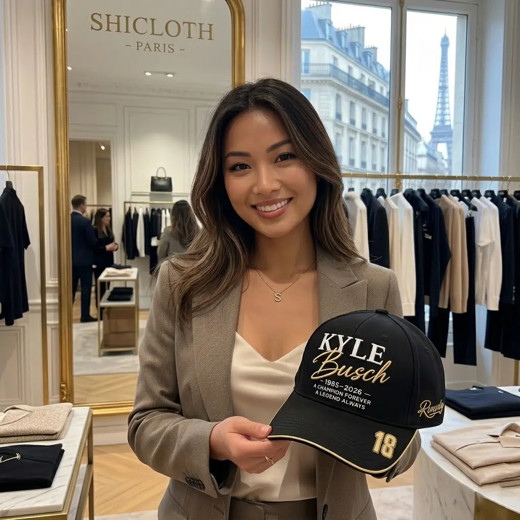 Woman holding a custom black Kyle Busch commemorative baseball cap in a Parisian boutique with the Eiffel Tower in the background.