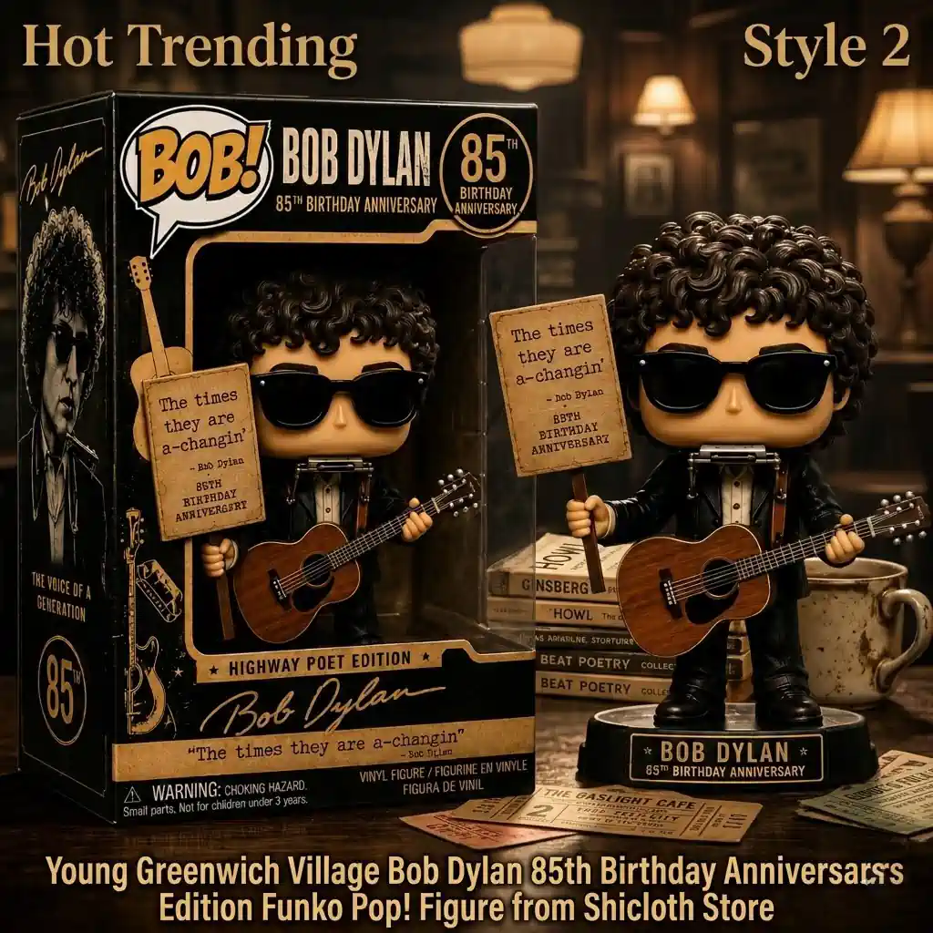 A Bob Dylan Highway Poet edition vinyl figure stands holding an acoustic guitar and a small sign! It is wearing dark sunglasses and a suit with a harmonica around its neck! A similar figure is inside its detailed collector box next to it! The set is on a wooden surface with a book titled Howl and other old items! The background shows vintage lamps!